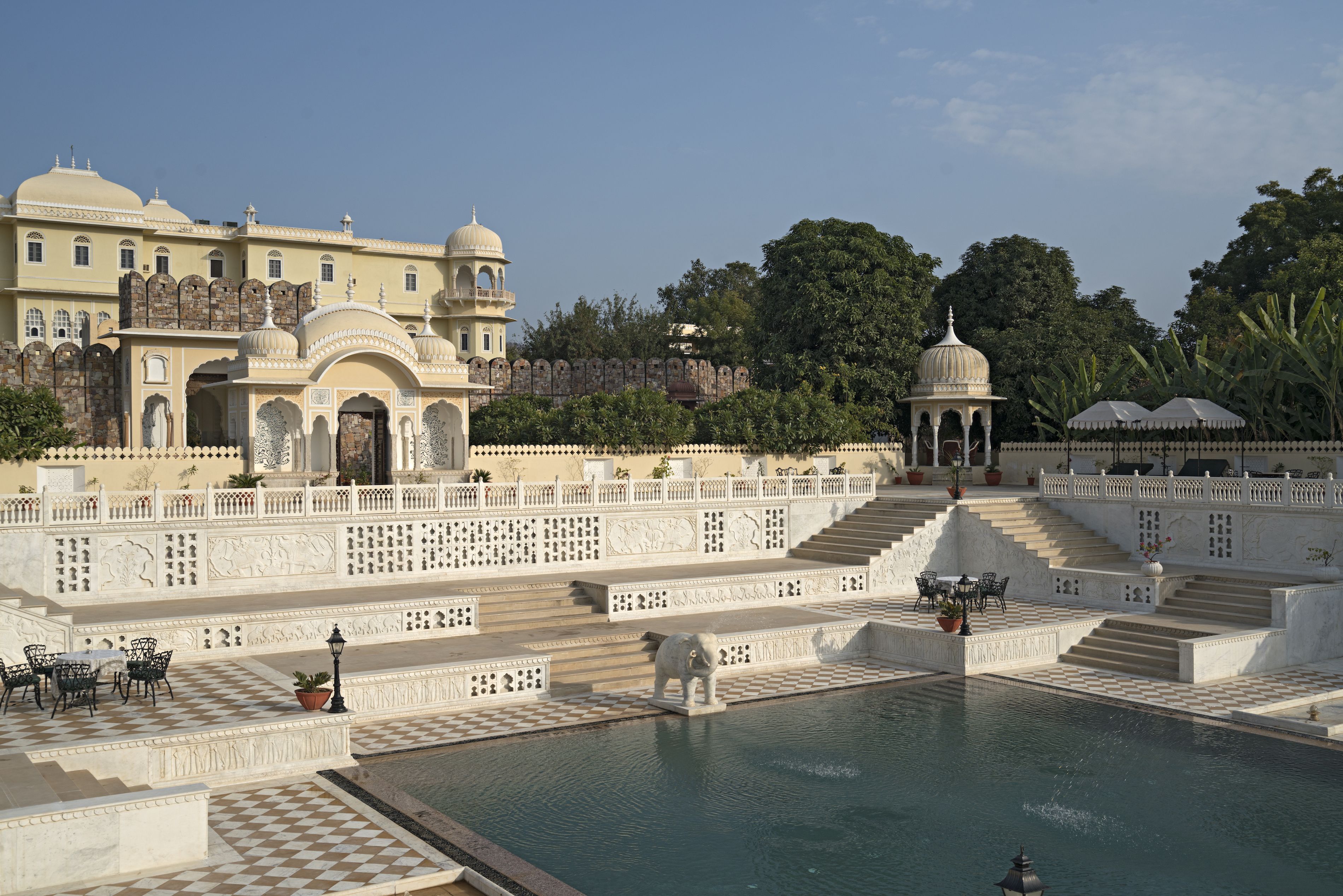 Un edificio imponente con numerose cupole e archi, una grande piscina con gradini e una recinzione decorata con motivi elaborati.