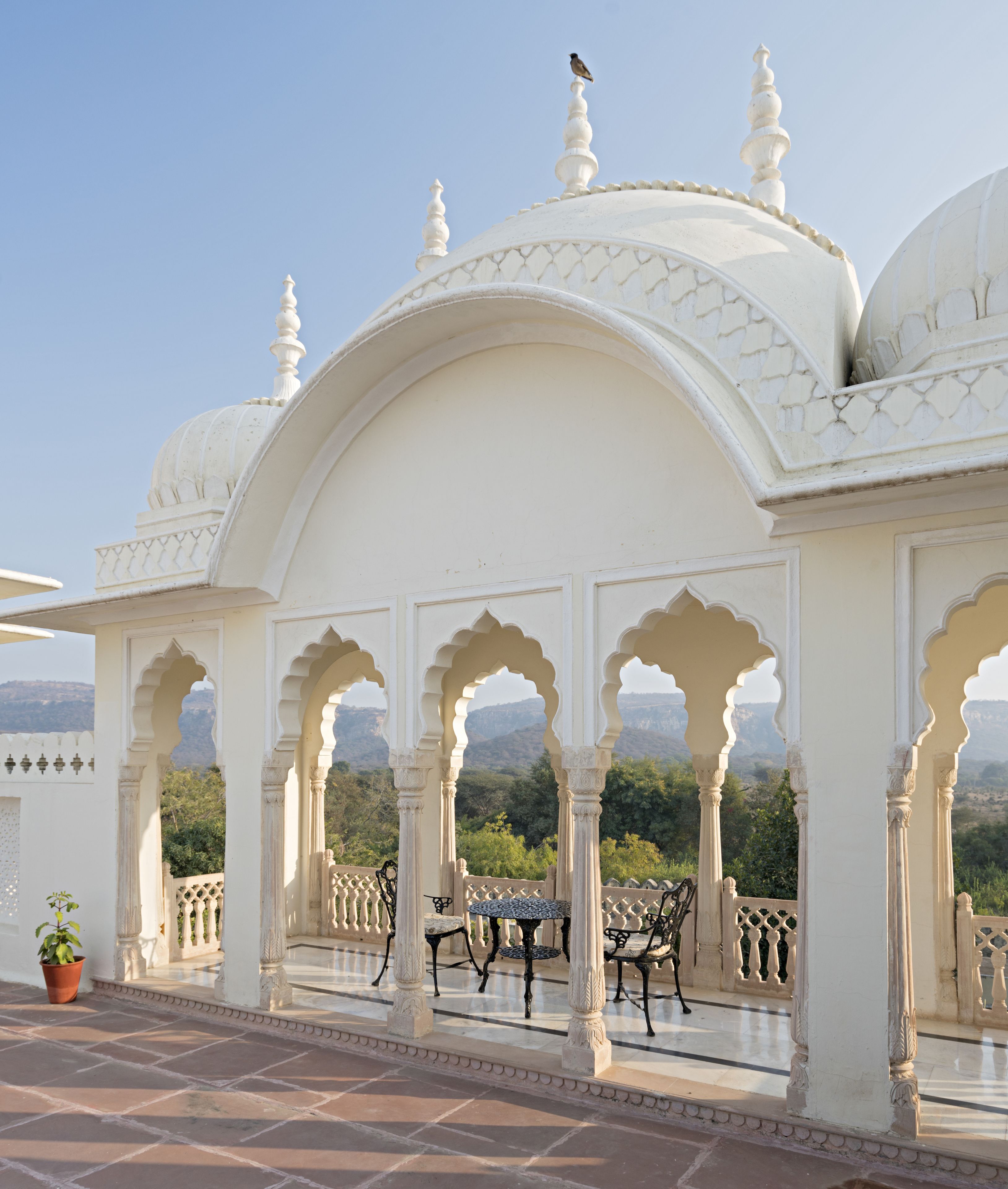 Ein weißes, verziertes Pavillon mit Bögen und einem Fliesenboden, mit Tisch und Stühlen.