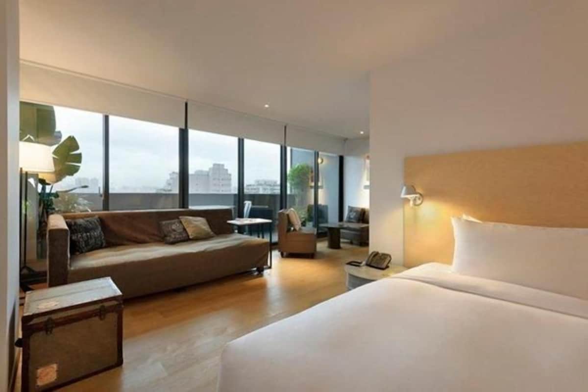 A modern hotel room with a large bed, a sofa, a small table, and a chair.