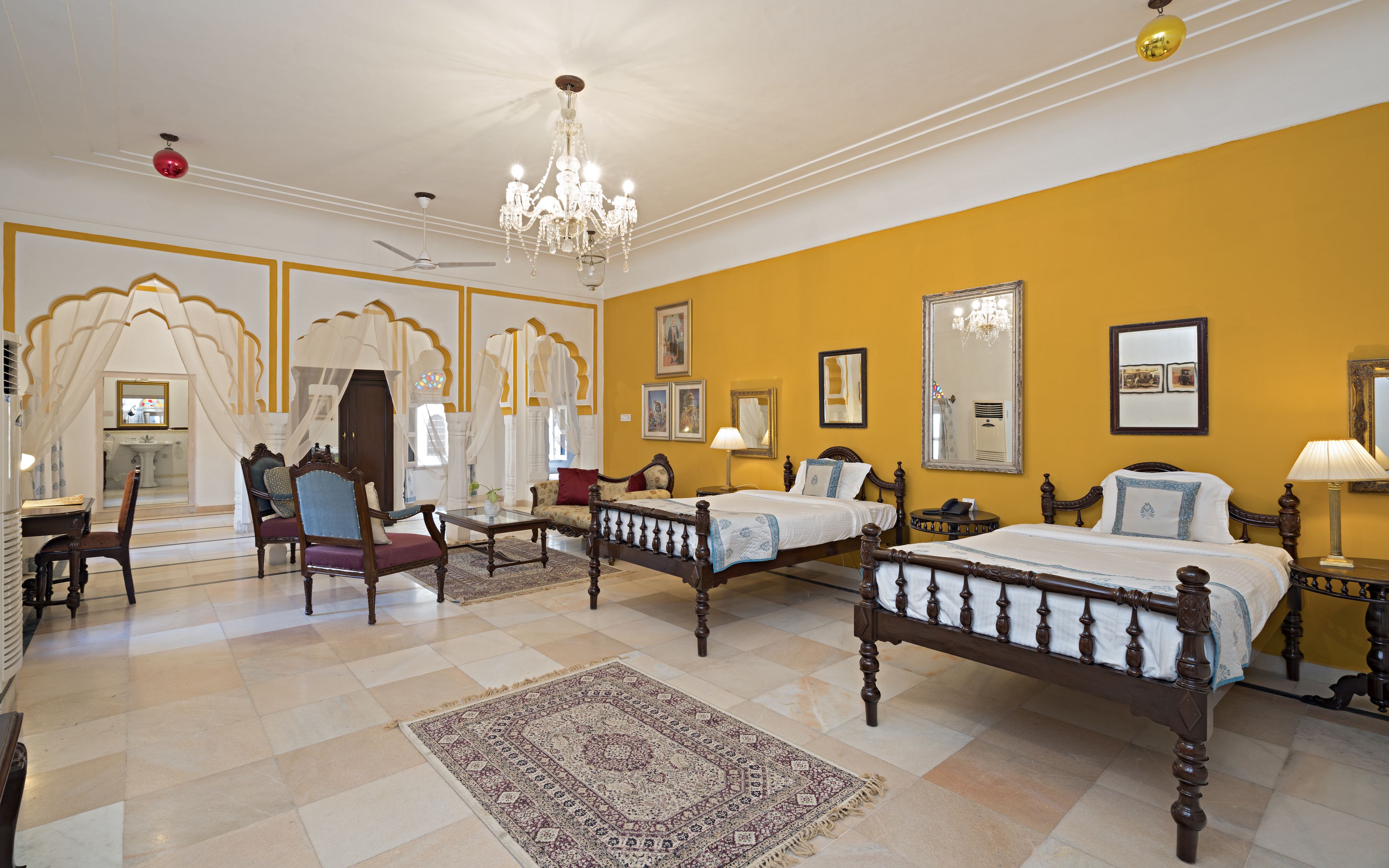 Camera d'albergo con due letti, un lampadario, uno specchio grande e un tappeto tradizionale.