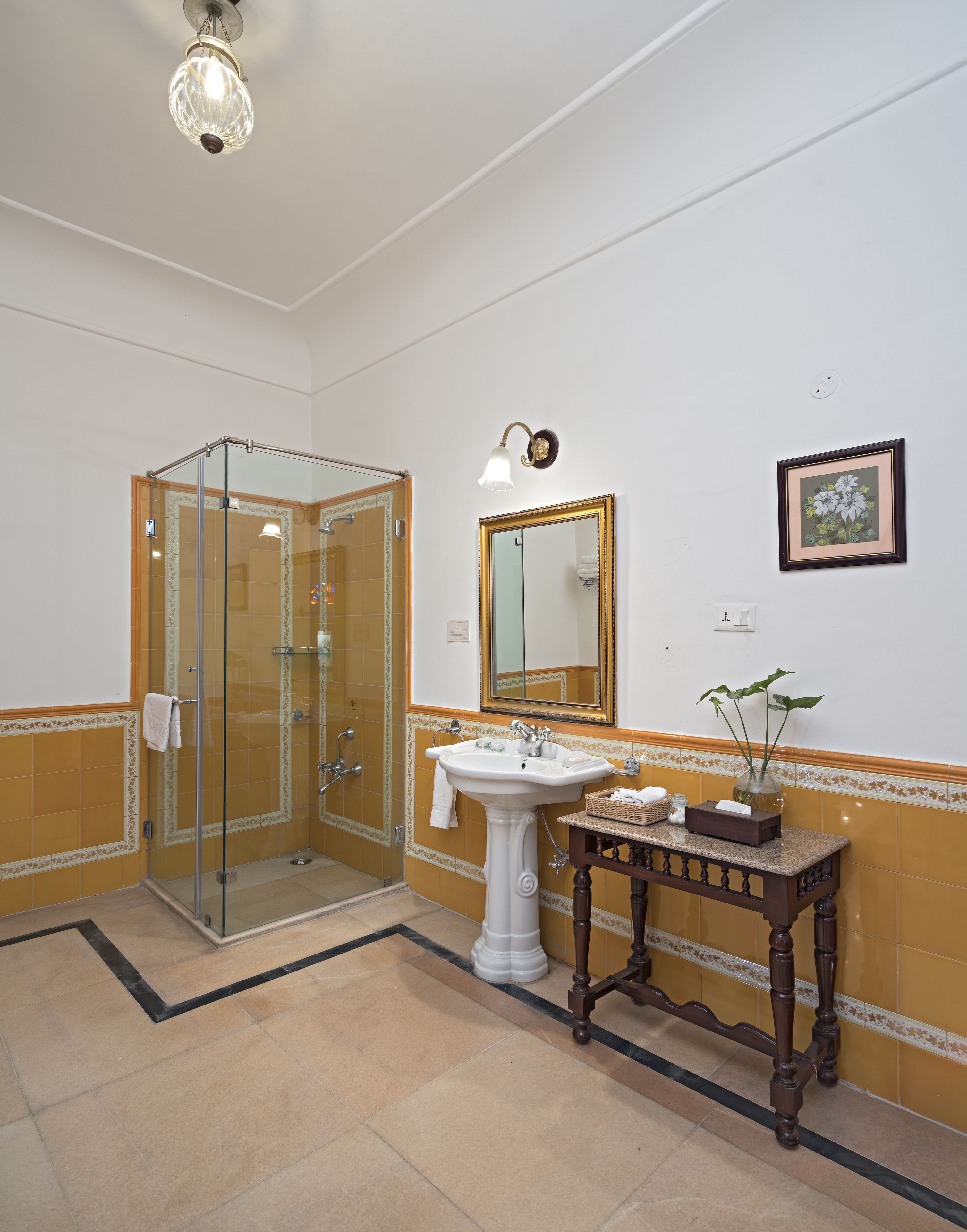 Ein Badezimmer mit Duschkabine aus Glas, einem Standwaschbecken, einem Waschtisch mit Spiegel und einem gerahmten Bild an der Wand.
