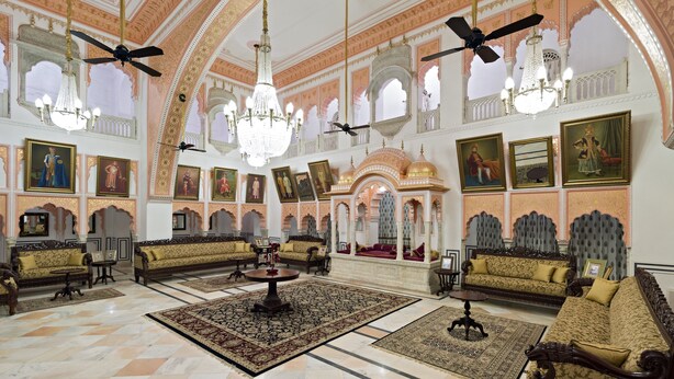 Un salón imponente con candelabros ornamentados, ventiladores de techo y arte tradicional.