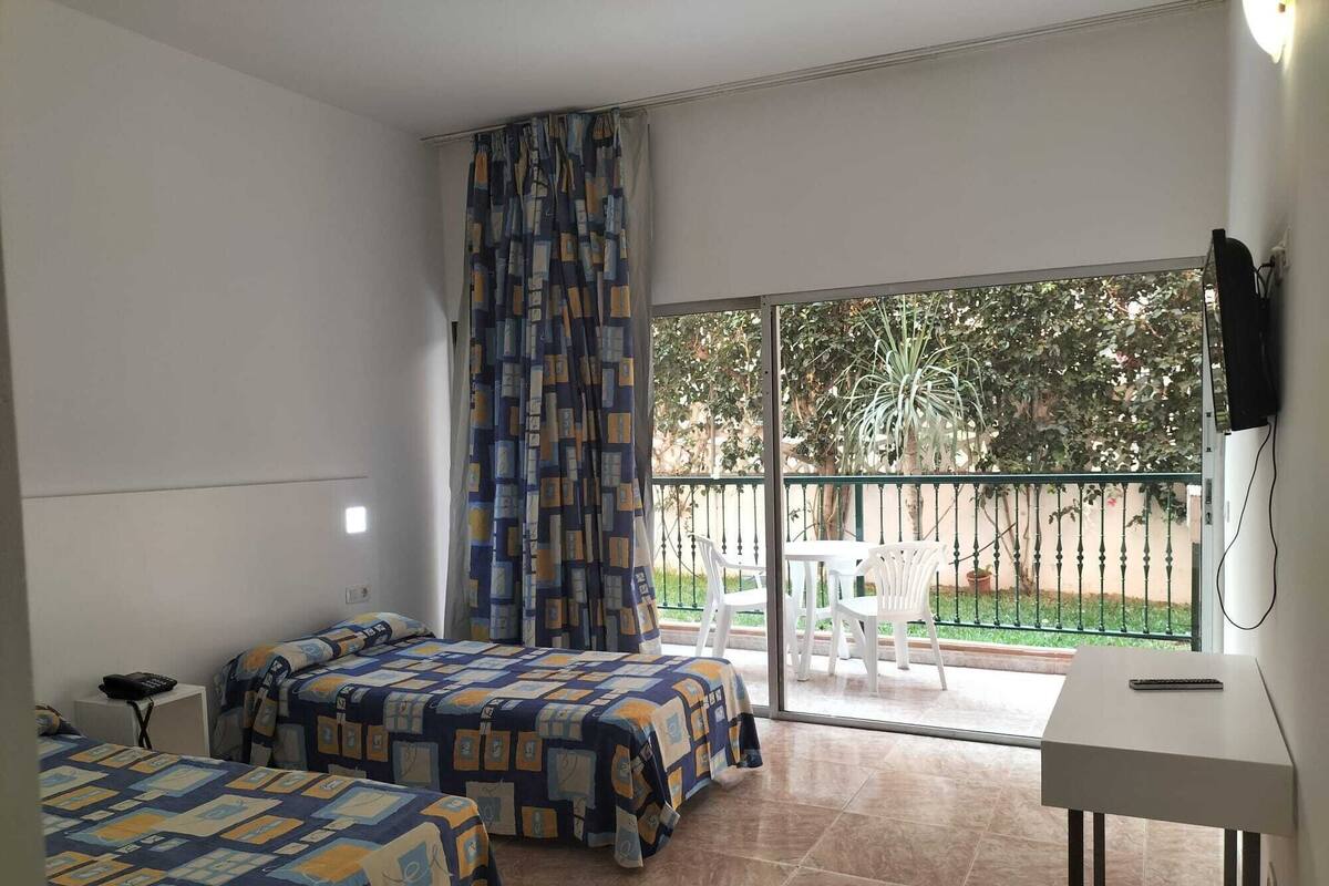 Une chambre avec deux lits, un bureau, une télévision et un balcon équipé d’une table et de chaises.