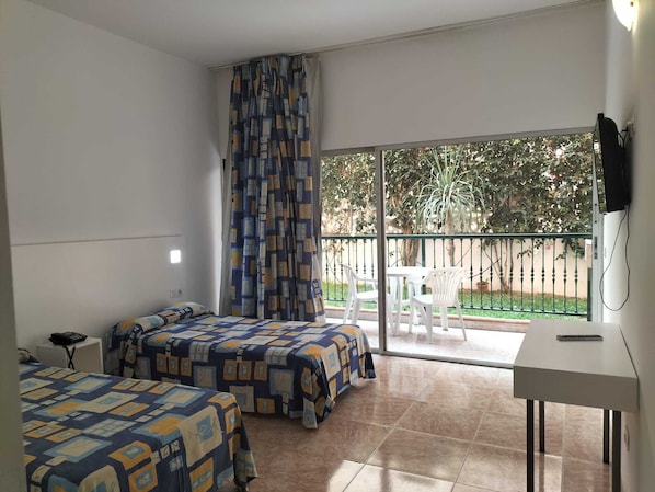 A room with two beds, a desk, a TV, and a balcony with a table and chairs.