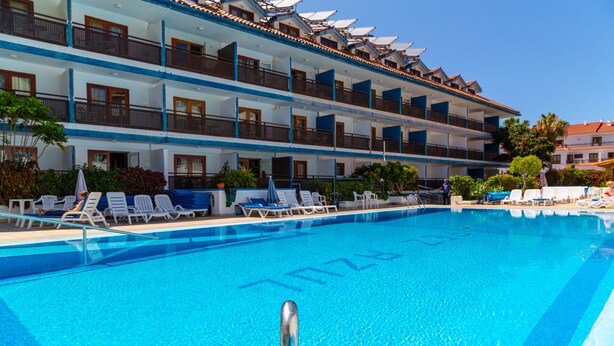 A hotel with a large swimming pool, multiple balconies, and outdoor seating areas.