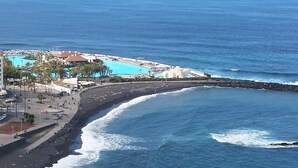 An aerial view of a coastal resort with a swimming pool, beach, and rocky shoreline.