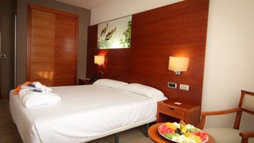 Habitación de hotel con cama, mesita de noche con frutero, una silla y cabecero de madera decorado con arte de pared.
