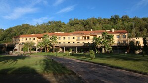 A large, multi-story hotel with a red-tiled roof, surrounded by lush greenery and a well-maintained lawn. - Balneario Valle del Jerte (Valdastillas)