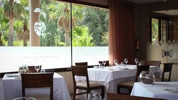 Un restaurante con mesas dispuestas para comer, ventanas amplias con vistas a palmeras y un letrero que dice 'Cocoon'.