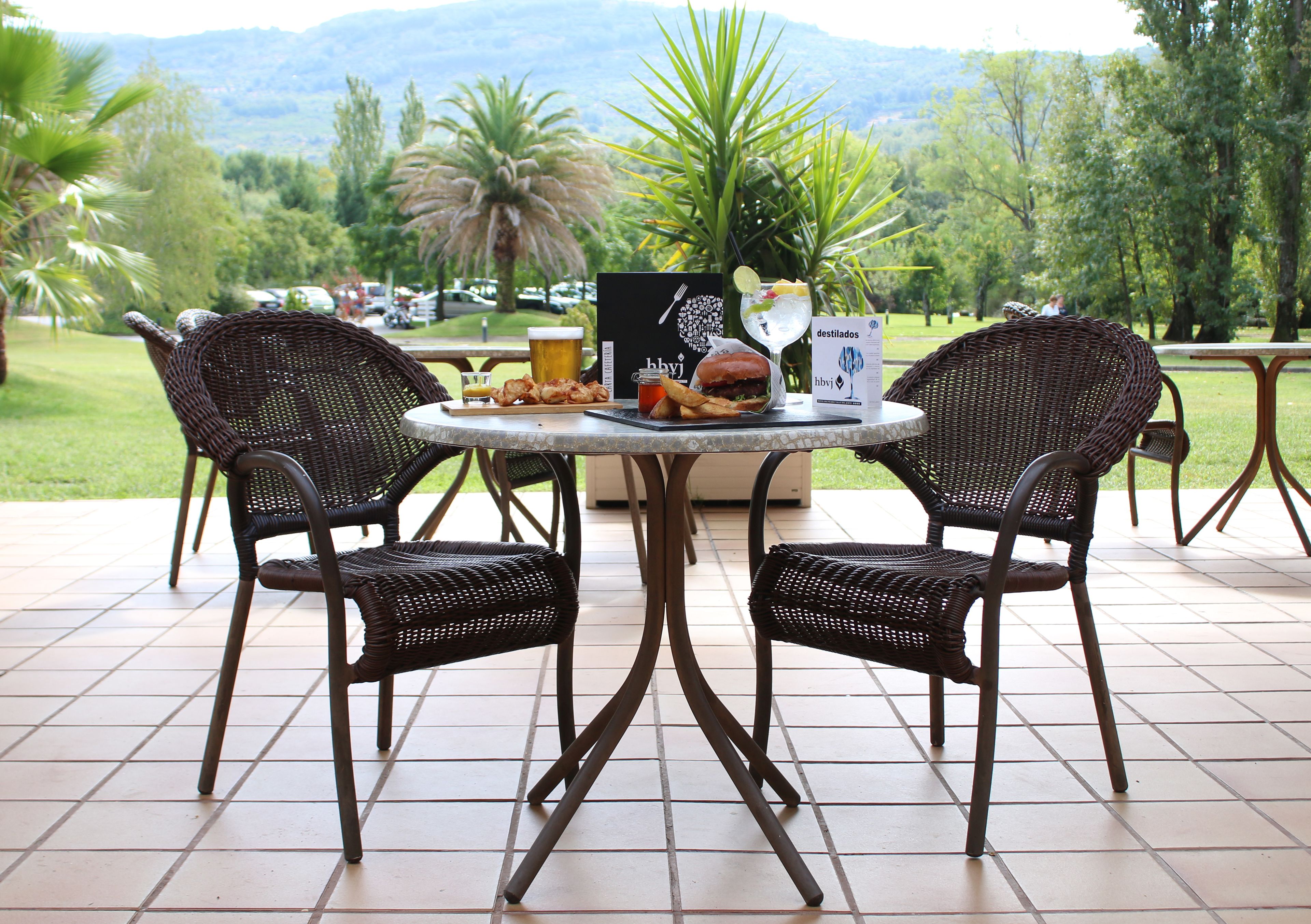 Una mesa en el patio con dos sillas de mimbre, una hamburguesa, papas fritas y una bebida.