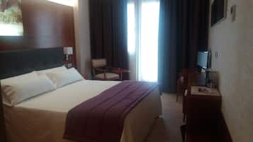 Habitación de hotel con una cama grande, un escritorio, una silla, un televisor y una ventana con cortinas.