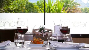 A dining table with wine glasses, a glass of water, and a plate of food, set against a backdrop of greenery and mountains. - Balneario Valle del Jerte (Valdastillas)