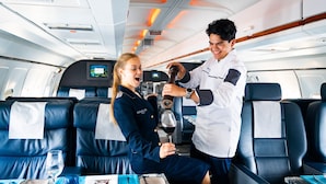 A cabin with leather seats, a small table with a wine glass, and a TV screen. - Novapark Das Flugzeughotel (Graz)