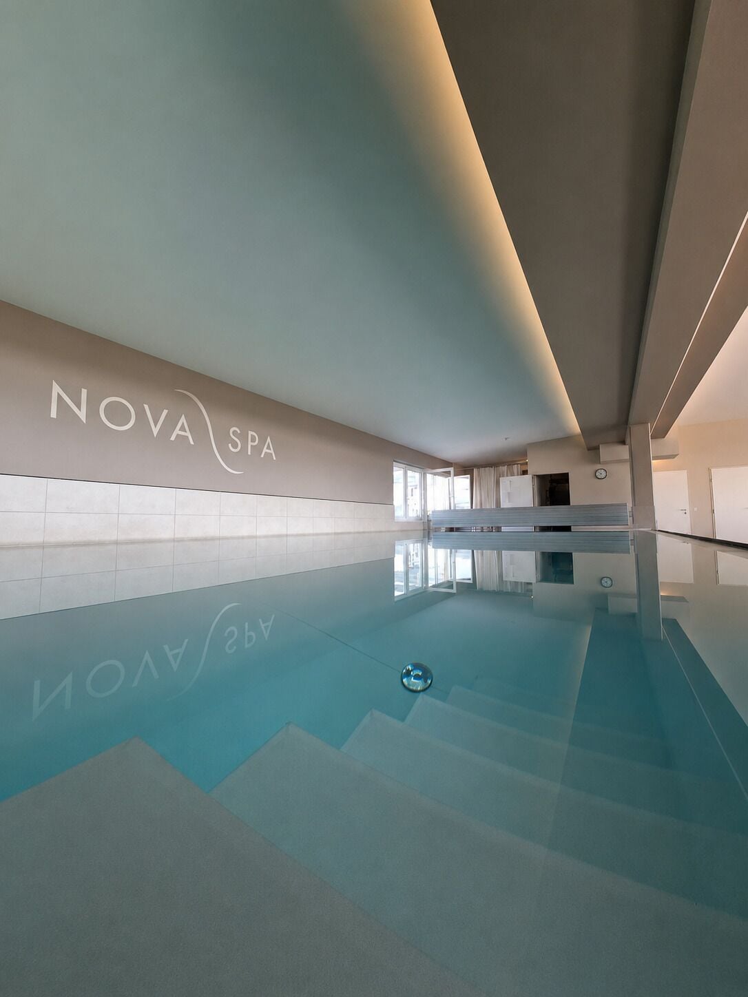 Ein modernes Hallenbad mit klarer Decke und einer Wand, auf der 'NOVA SPA' steht.