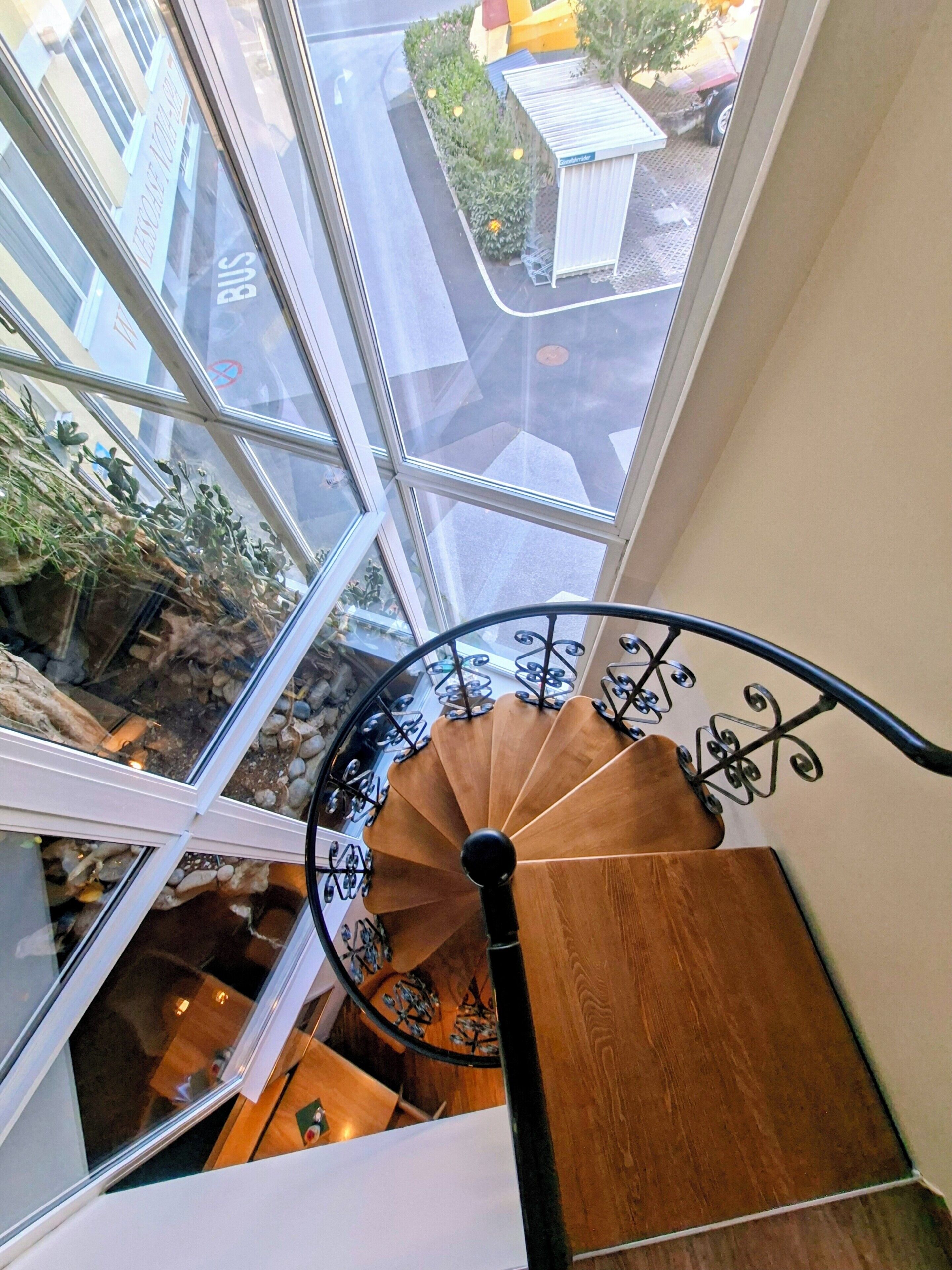 Eine Wendeltreppe mit Holzoptik und schwarzen Metallgeländern, die zu einer Ebene weiter unten führt.