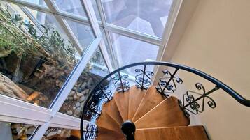Eine Wendeltreppe mit Holzoptik und schwarzen Metallgeländern, die zu einer Ebene weiter unten führt.