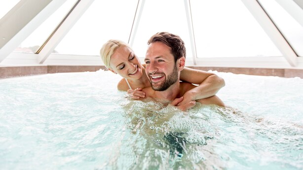 A couple in a hot tub with a high, white, triangular ceiling structure. - Novapark Das Flugzeughotel (Graz)