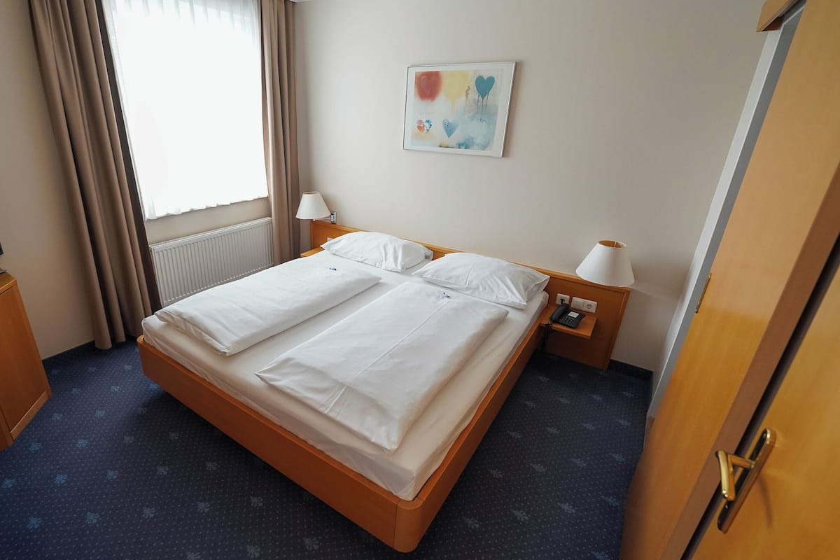 Habitación de hotel con una cama, televisión, lámpara y un cuadro en la pared.