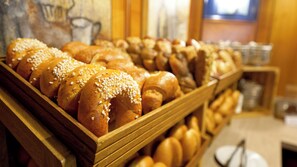 A wooden display case filled with various types of bread, including rolls and baguettes, in a bakery setting. - Novapark Das Flugzeughotel (Graz)