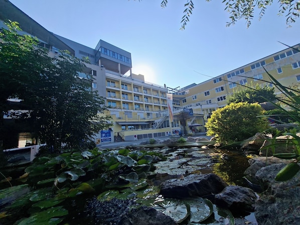 A building with multiple floors, a courtyard with a pond, and a clear sky.