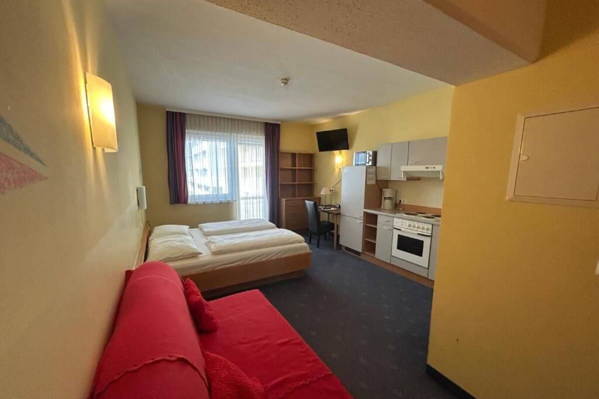 Una habitación de hotel compacta con cama, sofá, kitchenette y televisor.