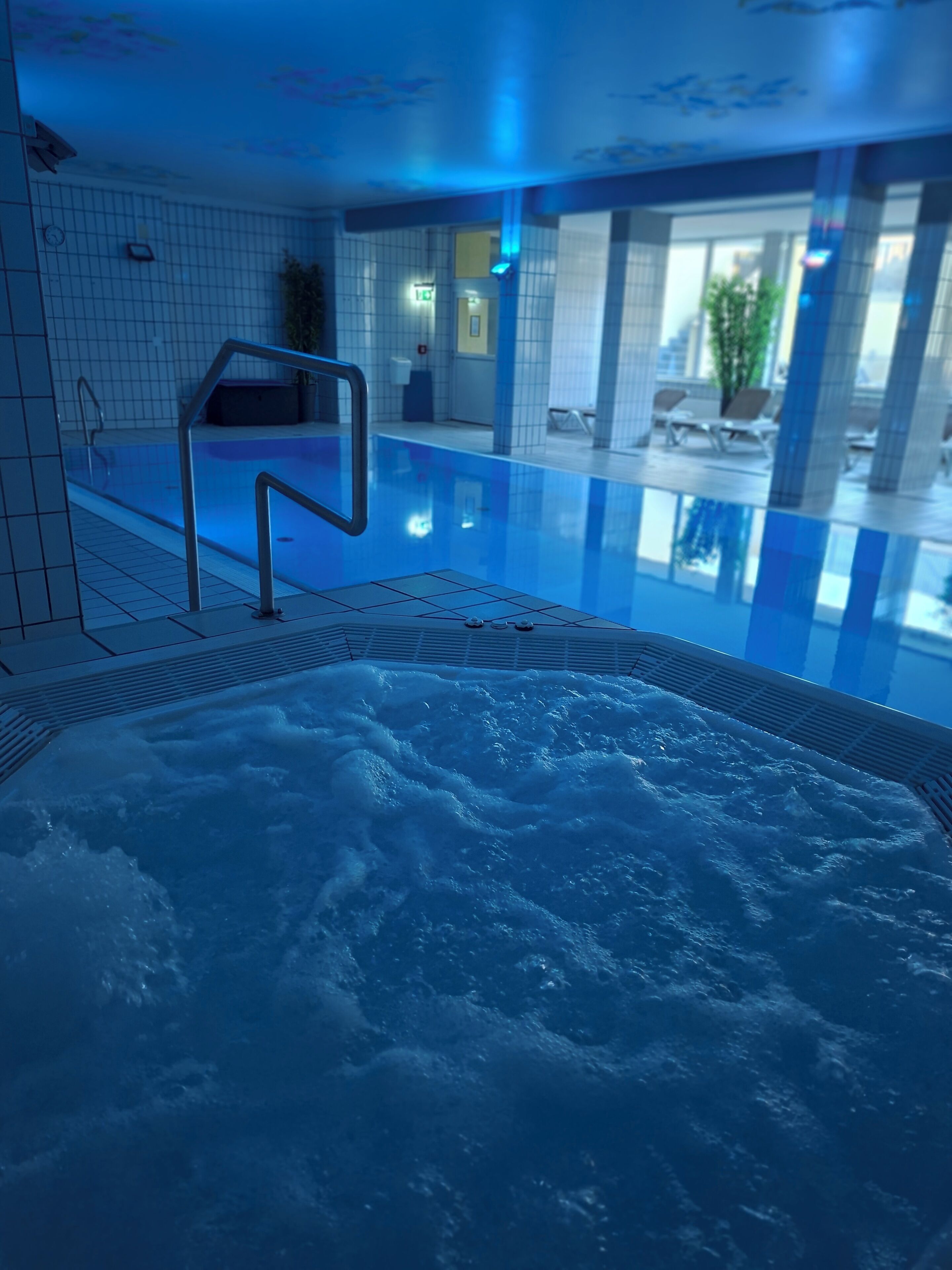 An indoor swimming pool with a hot tub area, tiled walls, and a clear view of the pool's edge.