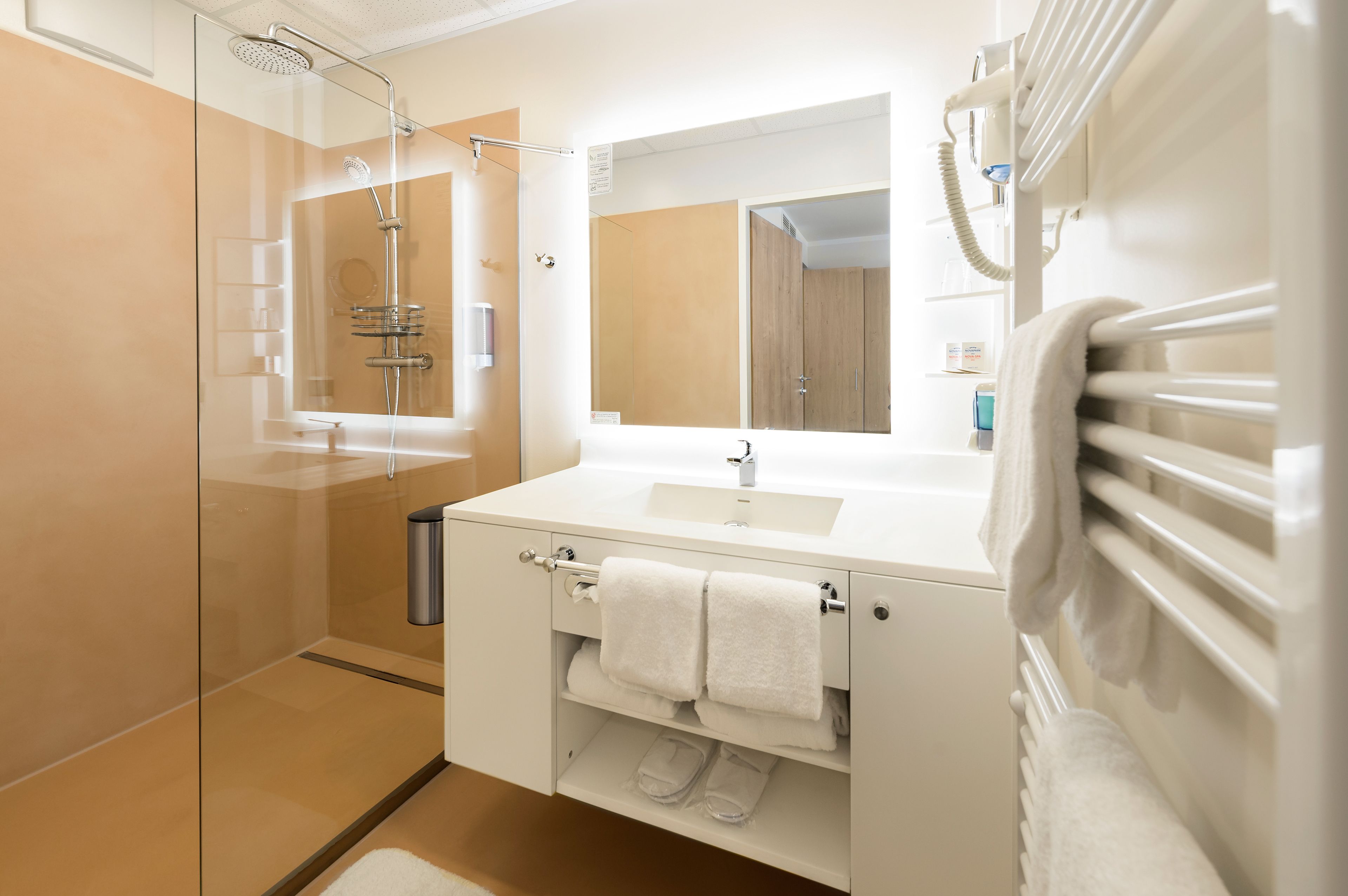 Ein modernes Badezimmer mit einer gläsernen Duschkabine, einem weißen Waschbecken und einem großen Spiegel.
