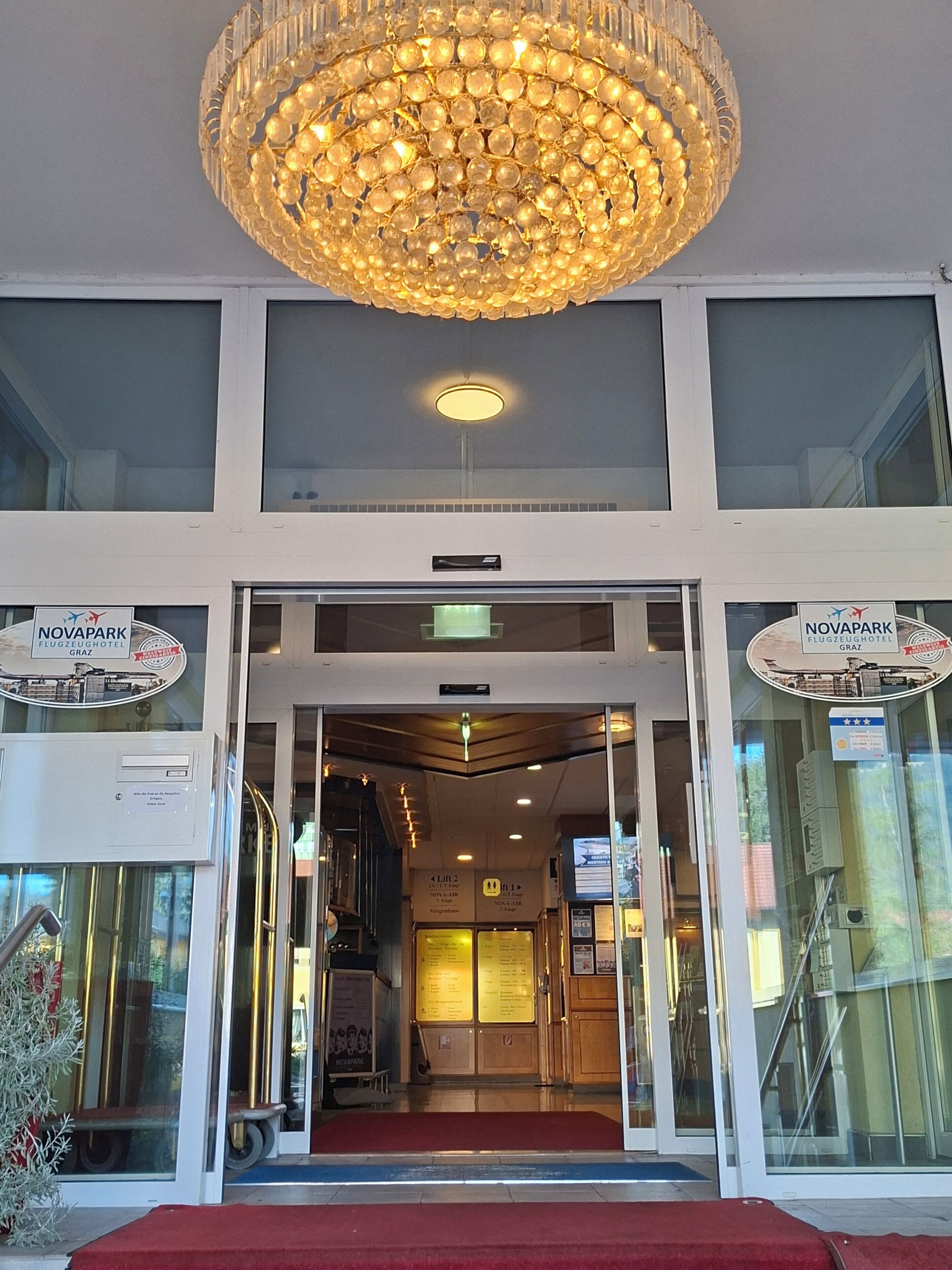 The entrance of a hotel with a chandelier, double doors, and a red carpet.