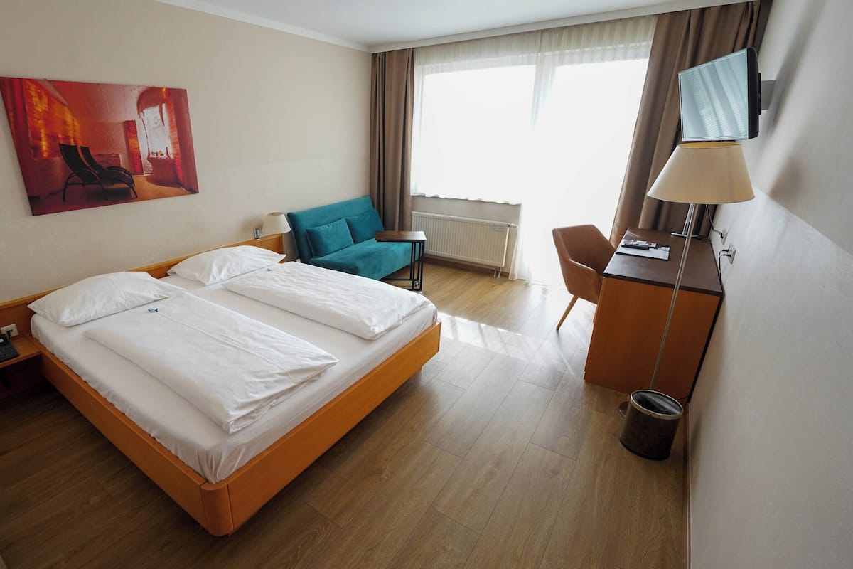 Una habitación de hotel con una cama grande, un escritorio con lámpara, una silla, un sofá y un cuadro en la pared.