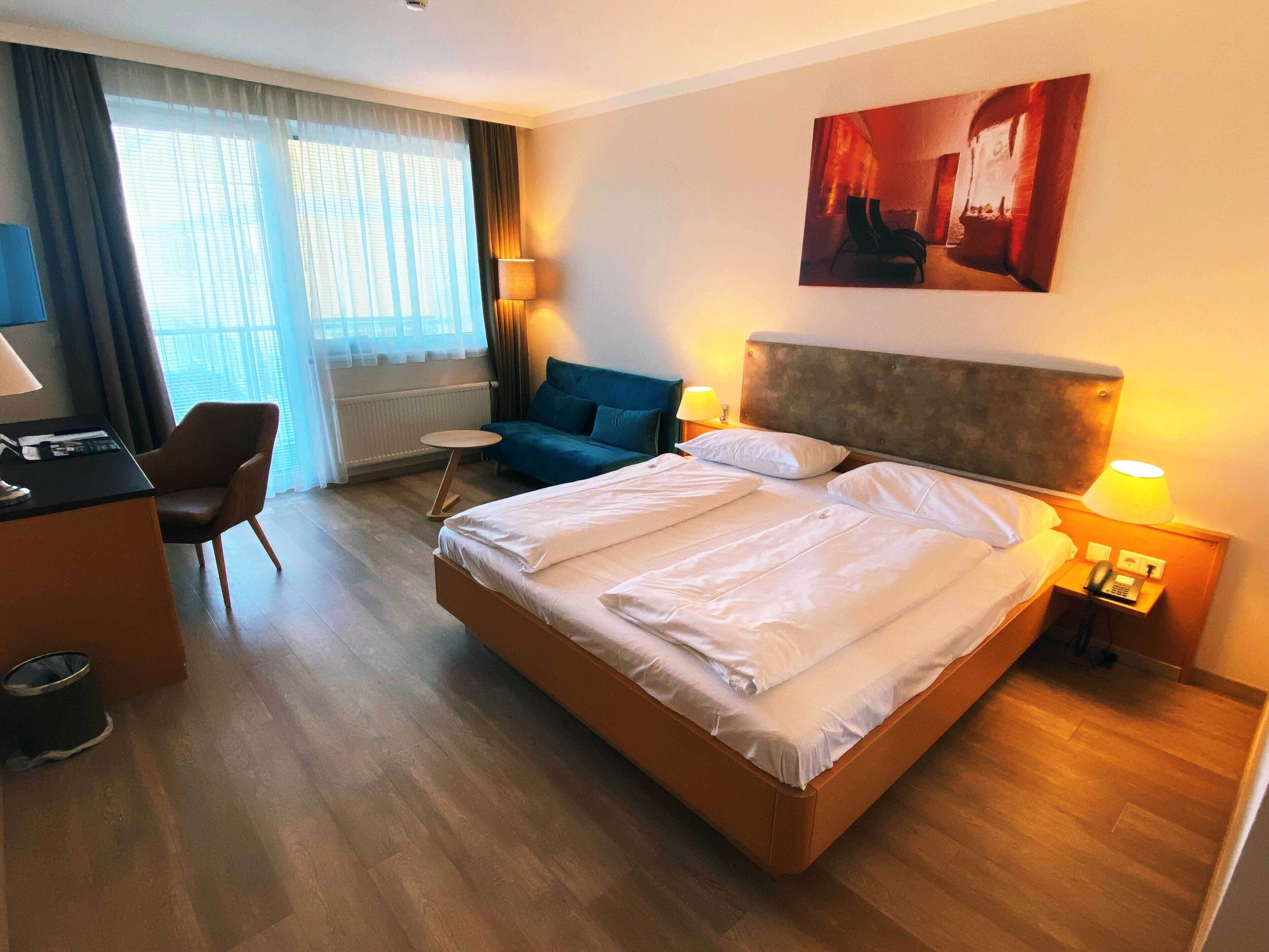 A hotel room with a large bed, a desk, a chair, a small table, and a couch.