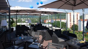 An outdoor patio with multiple tables and chairs, umbrellas, and a view of the cityscape. - Novapark Das Flugzeughotel (Graz)