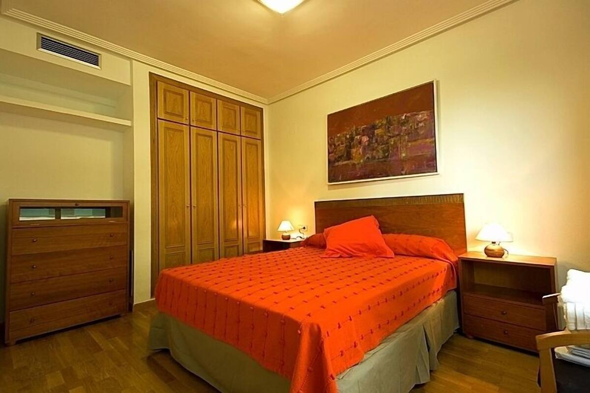 A bedroom with a large bed, wooden wardrobe, and a painting on the wall.