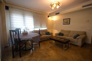 A living room with a dining table, two sofas, a chandelier, and a framed picture on the wall.