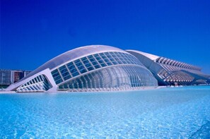 Une structure architecturale moderne dotée d’une façade incurvée en verre, située au bord d’une étendue d’eau d’un bleu limpide.