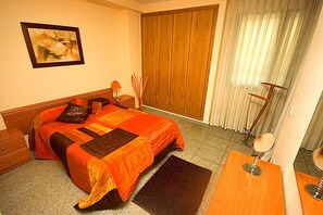 A bedroom with a bed, a wooden wardrobe, a mirror, and a painting on the wall.