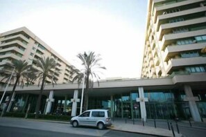 A modern building with a flat roof and multiple balconies. There are palm trees in front of the building.