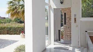 A modern entrance with a glass door, stone wall, and a small potted plant. - Pettas Apartments (Zakynthos)