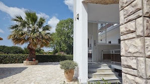 A modern building with a stone facade, a palm tree, and a potted plant in the foreground. - Pettas Apartments (Zakynthos)