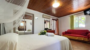 A hotel room with a bed, a red sofa, a mirror, and a window with curtains. - Pettas Apartments (Zakynthos)