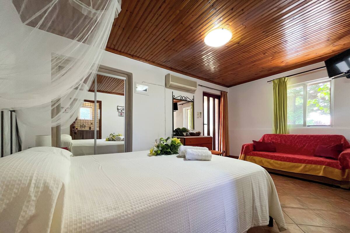 A hotel room with a bed, a red sofa, a mirror, and a window with curtains.