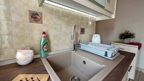 A kitchen with a sink, a dish rack, a kettle, and a bottle of dish soap. - Pettas Apartments (Zakynthos)