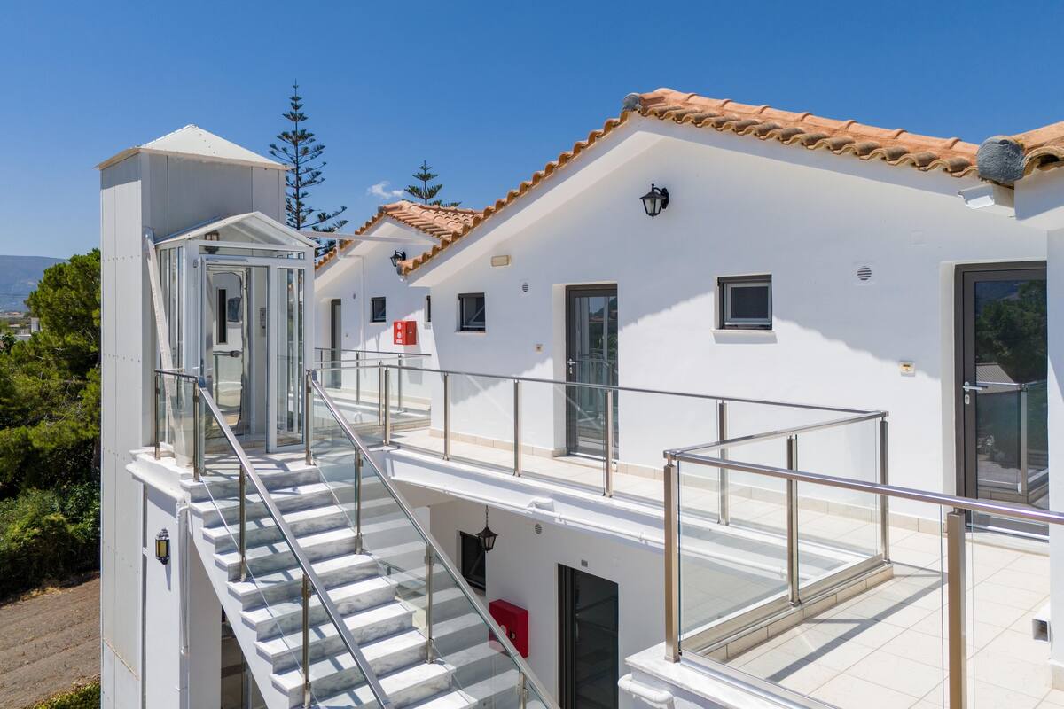 A modern building with a glass staircase leading to a balcony, white walls, and a tiled roof.