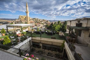 A courtyard with potted plants, outdoor seating, and a view of a historic town with a prominent tower. - Fresco Cave Suites & Mansions - Special Class (Ürgüp)