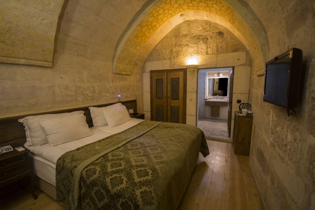 Un dormitorio con cama, cabecera de madera y un arco de piedra.