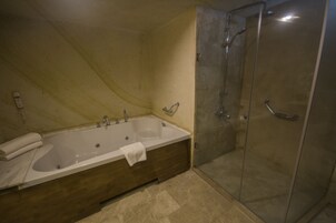 Un baño con una bañera grande, un box de ducha de vidrio y un tocador de madera.