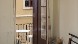 Un dormitorio con cama, una mesita de noche con un florero y vistas a un balcón exterior con mesa y sillas.