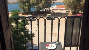 Un balcon avec vue sur la mer, les arbres et une voiture garée.