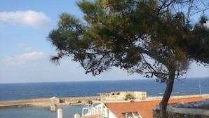 Un pueblo costero con edificios de tejas rojas, un muro de piedra y vistas al mar.