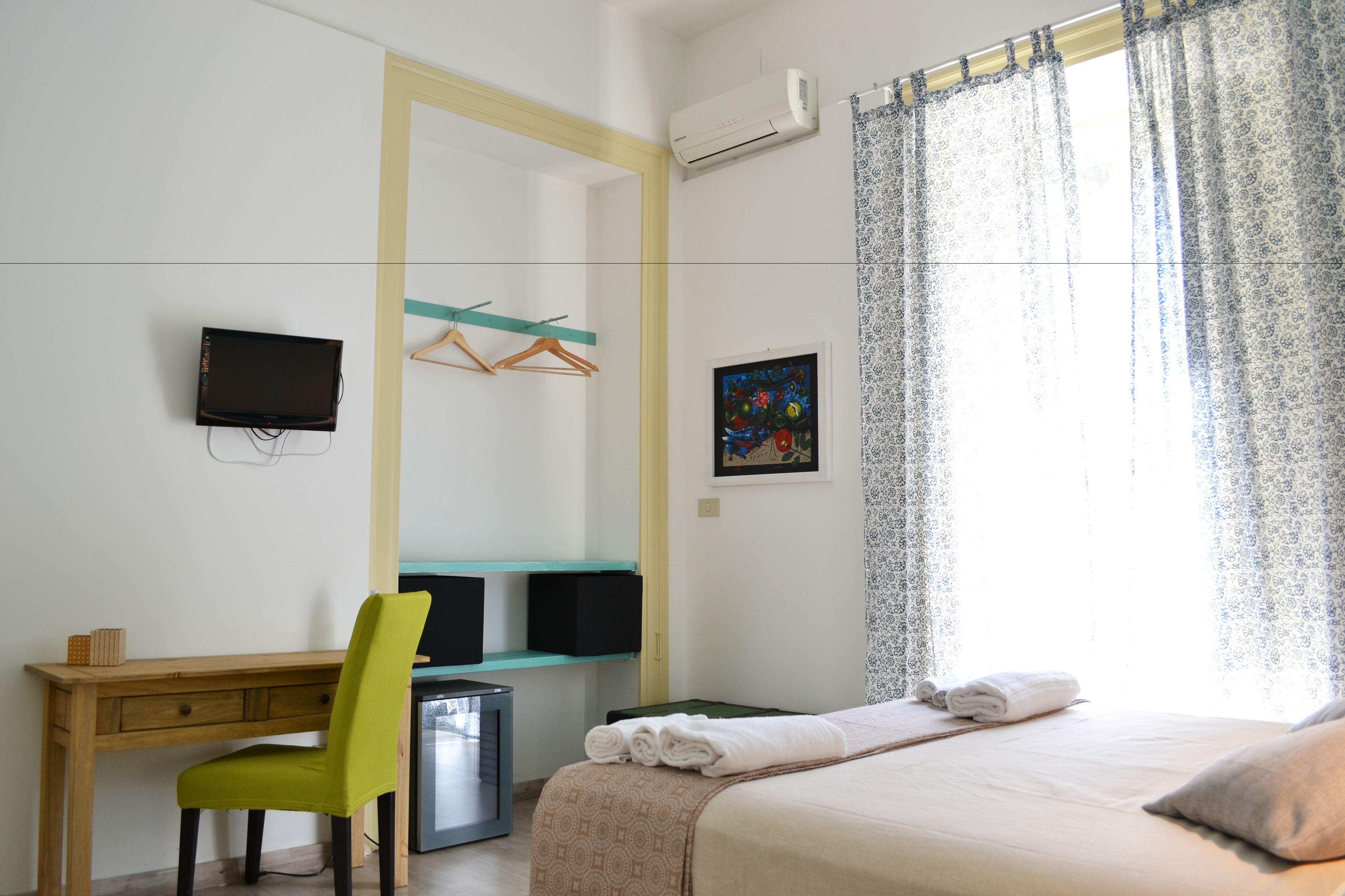 Ein Hotelzimmer mit Bett, Schreibtisch, Stuhl, Fernseher und einem fenster mit Vorhängen.