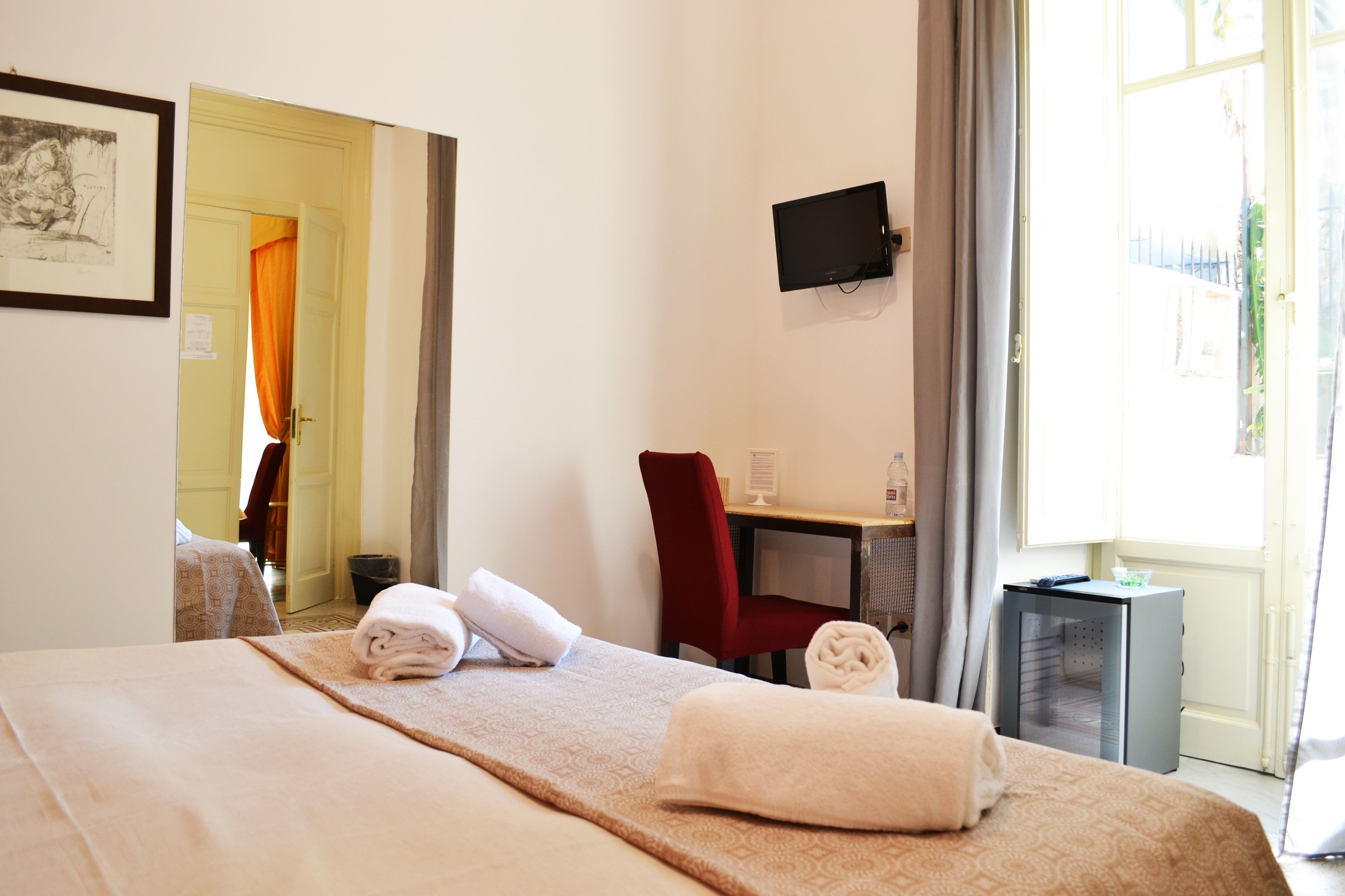 A hotel room with a bed, a desk, a chair, a TV, and a window.